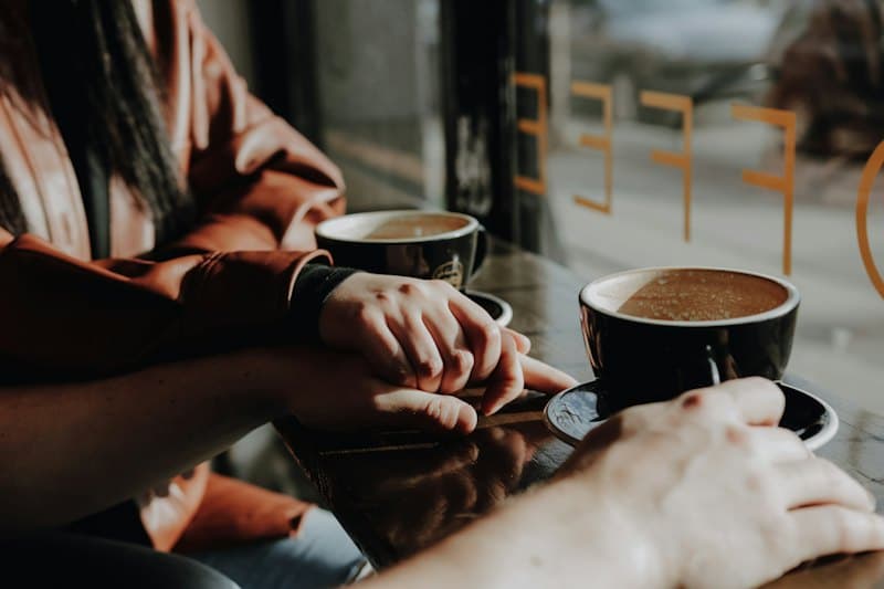 Hai người ngồi bên cửa kính, hai tách cà phê trên bàn gỗ